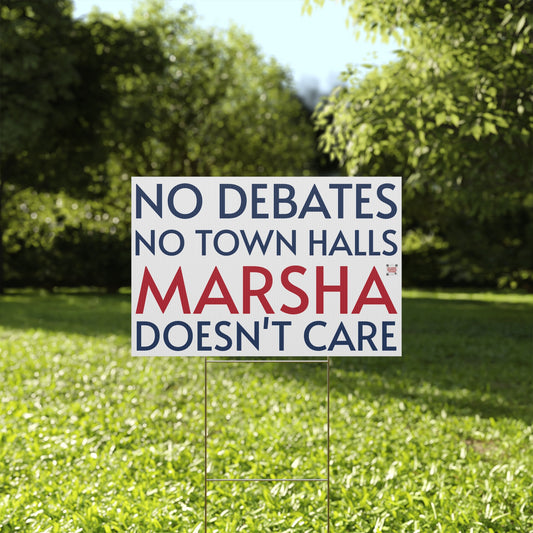 Political sign on grass with text 'No debates, no town halls, Marsha doesn't care' in a park setting.