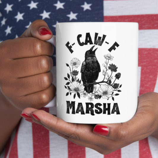 Black woman holding a mug with a black crow sitting on a black and white wildflower branch on a white background and  with 'F-CAW-F Marsha' in black text, wearing an American flag t-shirt.